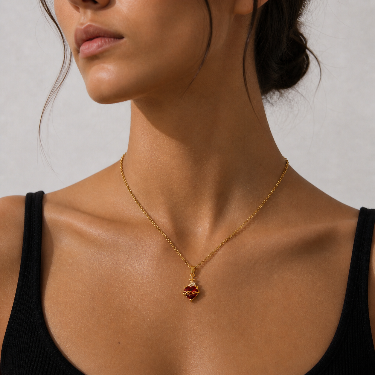 Close-up of a woman wearing a gold necklace with a red pendant against a neutral background