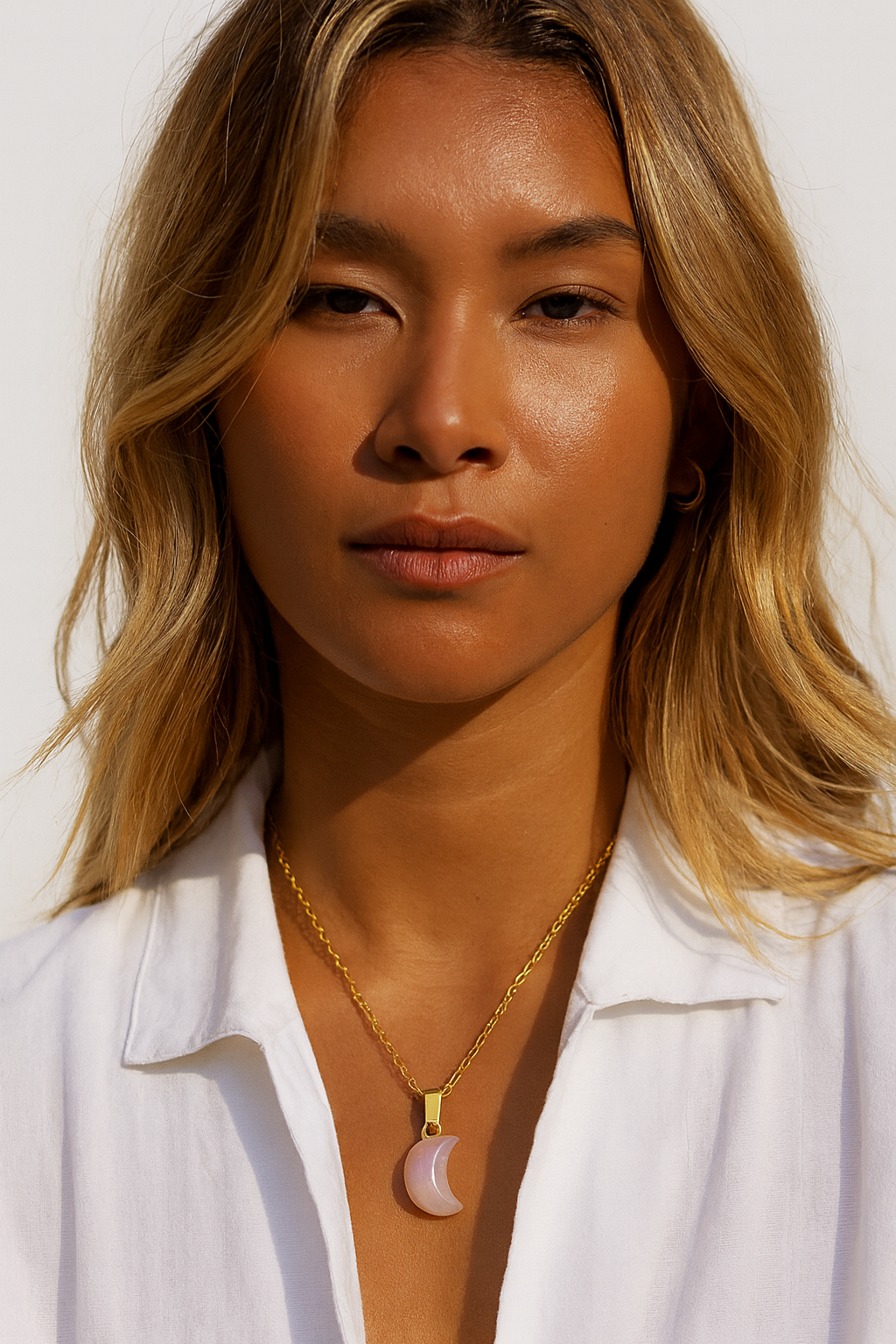 Woman wearing a gold necklace with a moon pendant against a white background