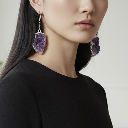Close-up of a woman wearing purple amethyst earrings against a neutral background
