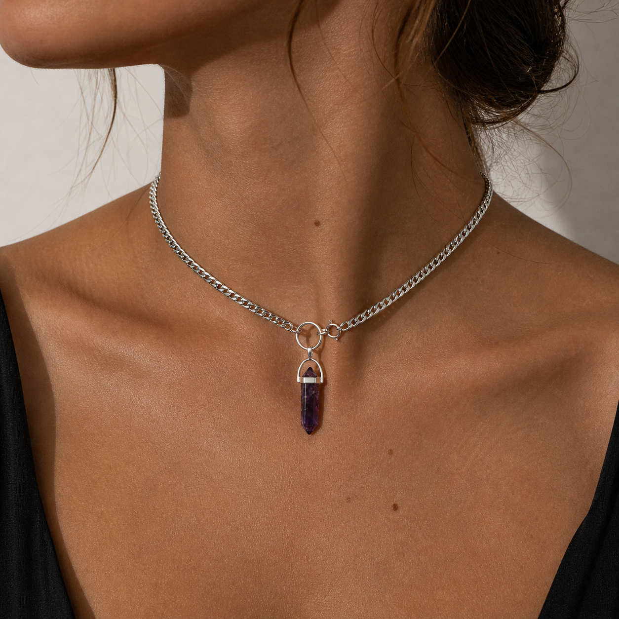 Necklace with a purple pendant worn by a person against a neutral background