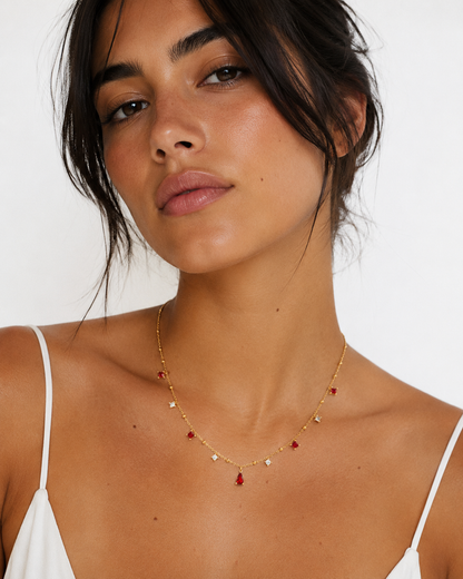Woman wearing a delicate gold necklace with small red beads against a plain background