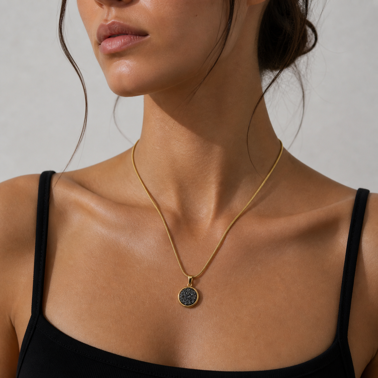 Woman wearing a gold necklace with a dark pendant against a neutral background