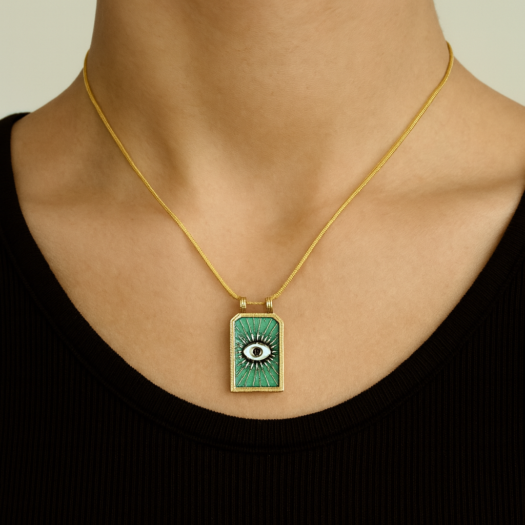 Gold necklace with a green pendant featuring an eye design on a neutral background