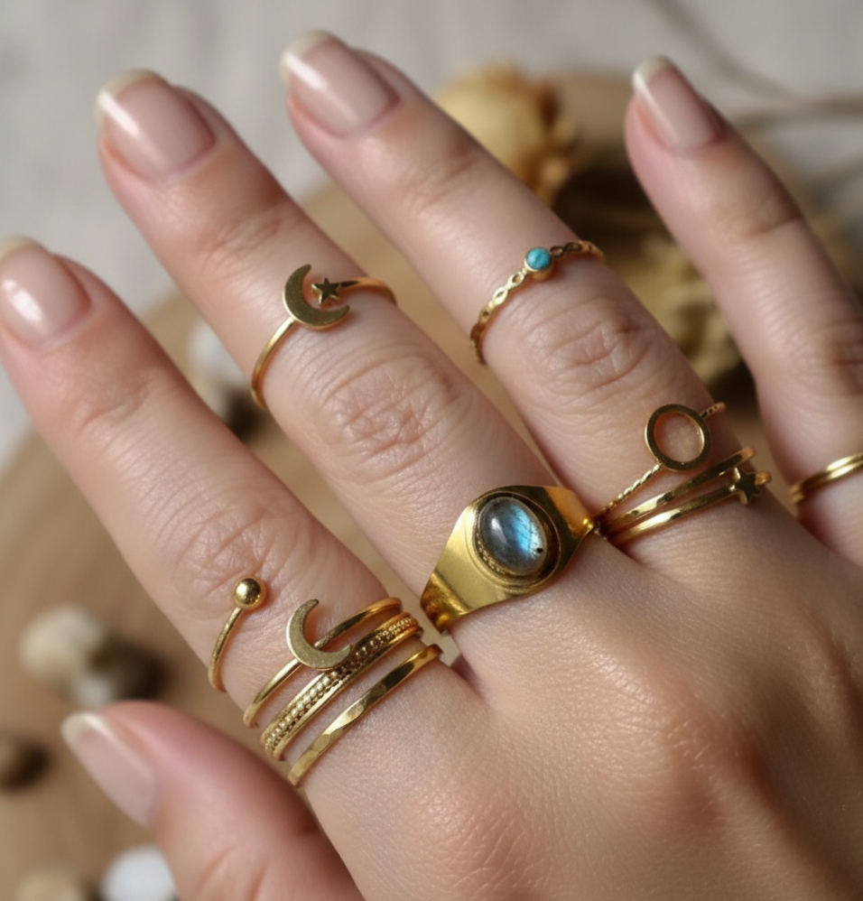 Hand wearing multiple gold rings with gemstones on a neutral background