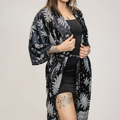 Woman wearing a black floral kimono over a black outfit on a plain background